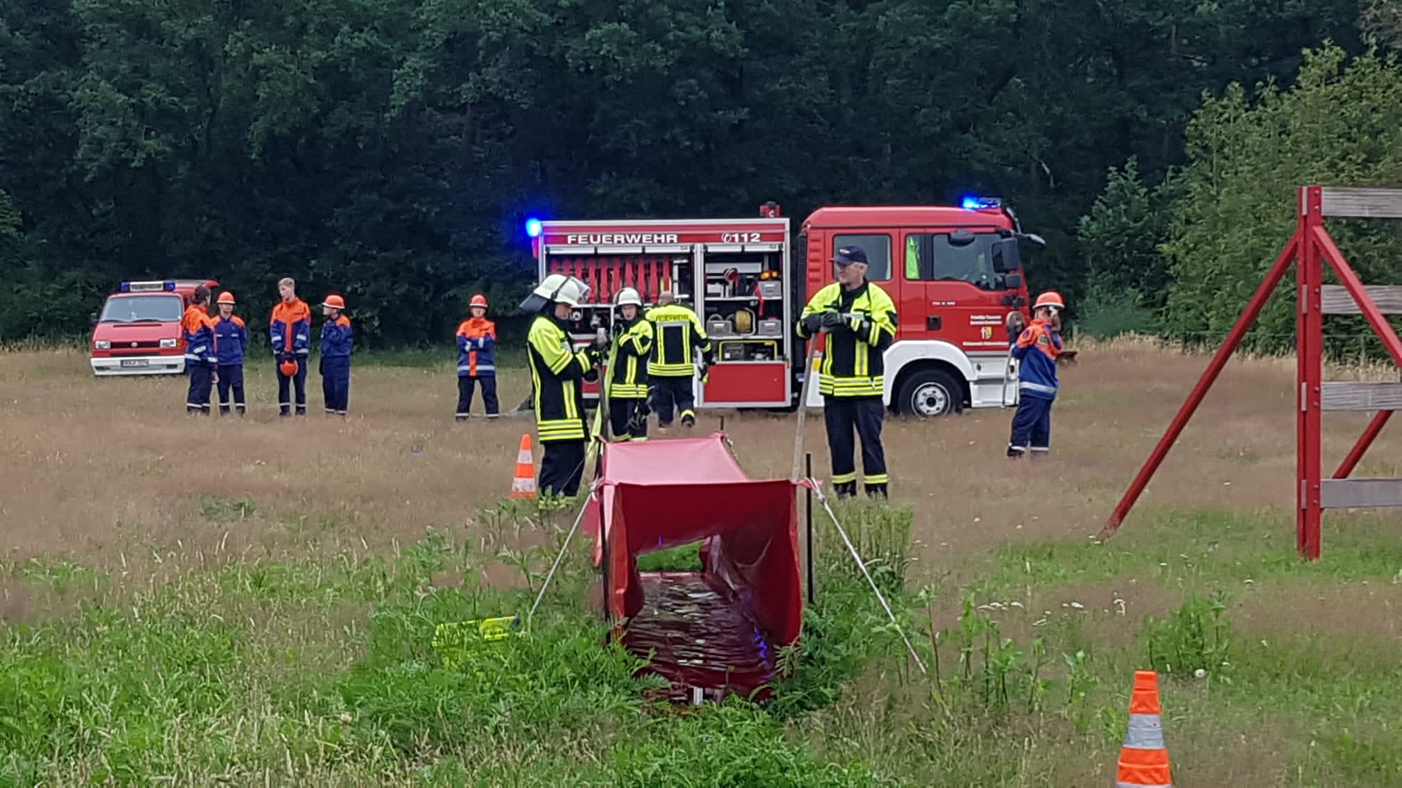 Übung Jugendfeuerwehr auf einer Wiese mit Unterstützung von aktiven Kameraden