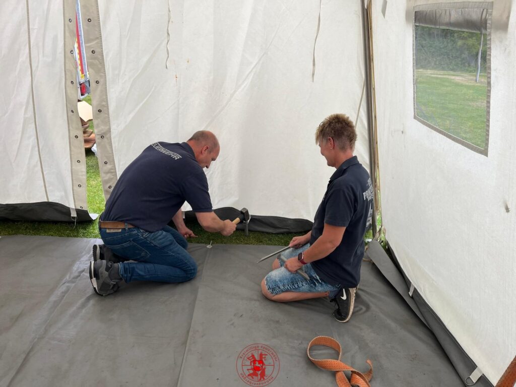 es wird der Boden im Zelt verlegt und Heringe in den Boden geschlagen